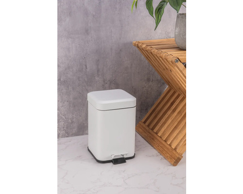 Poubelle à pédale blanche en métal à côté d''une table d''appoint en bois