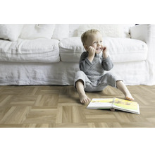 Un enfant est assis avec un livre sur un parquet devant un canapé