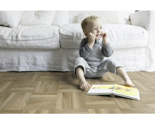 Un enfant est assis avec un livre sur un parquet devant un canapé