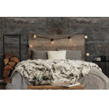 Schlafzimmer mit Bett, Holzkopfende, Lichterkette und dekorativen Elementen wie Holzstapel und Fellimitatdecke.