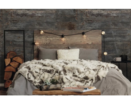 Schlafzimmer mit Bett, Holzkopfende, Lichterkette und dekorativen Elementen wie Holzstapel und Fellimitatdecke.