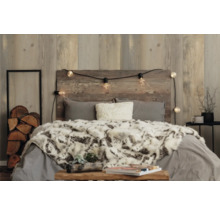 Chambre avec mur en bois, lit, couverture, coussins et guirlande lumineuse