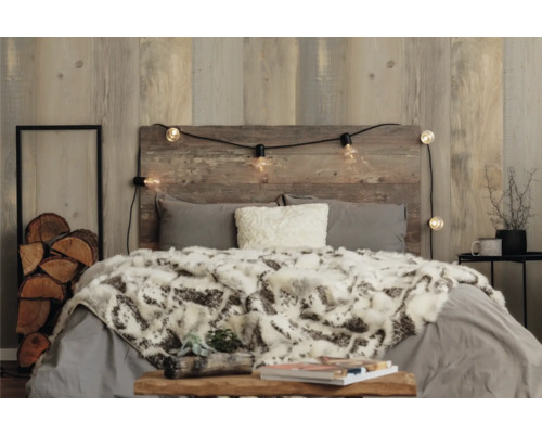 Schlafzimmer mit Holzwand, Bett, Decke, Kissen und Lichterkette