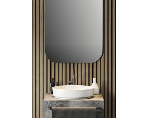 Badezimmerwaschbecken mit Spiegel, Armatur, Handtuchhalter und Dekorationsartikeln vor einer Holzpaneelwand.