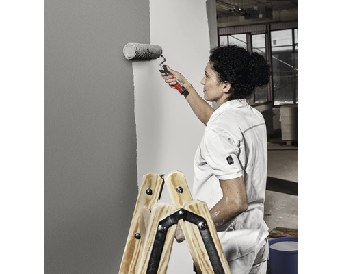 Femme peignant un mur avec un rouleau à peinture debout sur une échelle