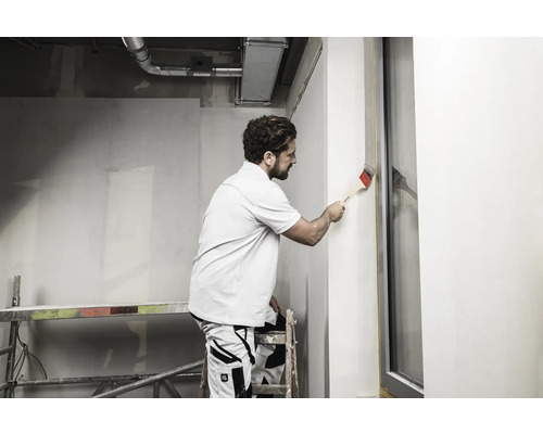 Un homme peint un mur avec un pinceau sur un chantier