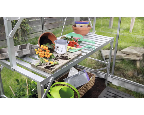 Serre avec table de plantation, pots et outils de jardinage.