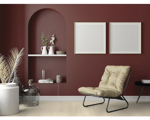 Wohnzimmer mit Sessel, Dekoration und Bilderrahmen an einer dunkelroten Wand