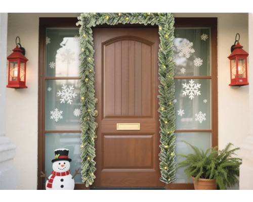 Entrée de maison décorée avec une guirlande de sapin, des lanternes et un bonhomme de neige
