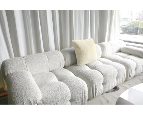 Modulares Sofa mit Kissen und Polsterstruktur vor einem Fenster mit Vorhang