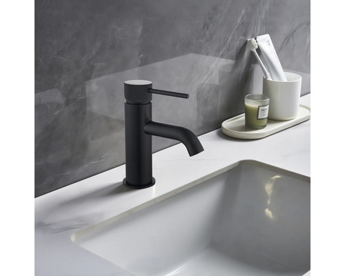 Schwarzer Waschtischmischer neben weissem Waschbecken und Badutensilien