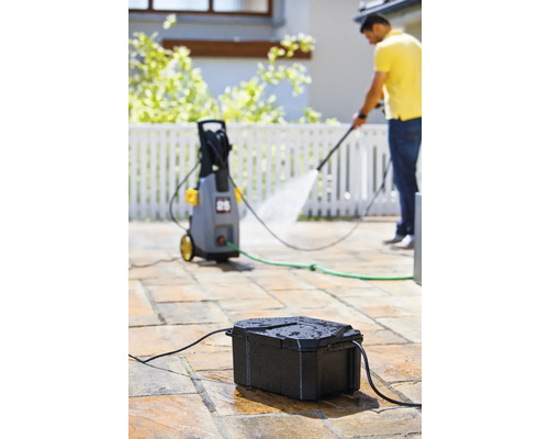 Scène avec nettoyeur haute pression, boîtier de raccordement d''eau et personne effectuant des travaux de nettoyage à l''extérieur.