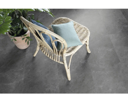 Szene mit einem Rattansessel mit Kissen und einer Topfpflanze auf einem grauen Bodenbelag.