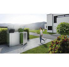 Box à poubelles en métal avec deux poubelles et une femme avec un râteau dans le jardin