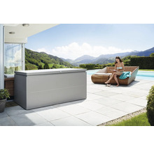 Scène d''extérieur avec un grand coffre de rangement à côté d''une femme assise sur un canapé au bord d''une piscine, avec vue sur un paysage montagneux