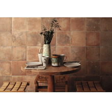 Dekoratives Esszimmer mit Keramikfliesen an der Wand, einem runden Holztisch, Geschirr und zwei Hockern