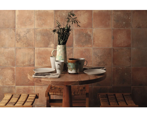 Dekoratives Esszimmer mit Keramikfliesen an der Wand, einem runden Holztisch, Geschirr und zwei Hockern