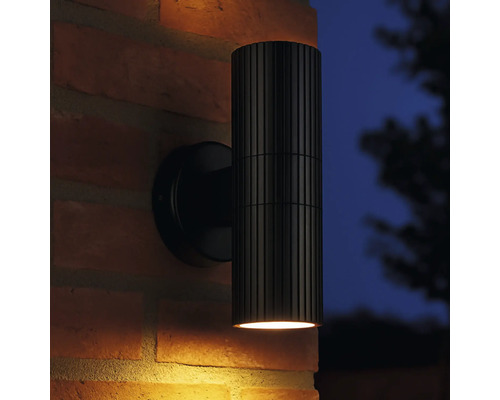 Applique murale extérieure noire avec corps de lampe nervuré sur un mur en briques