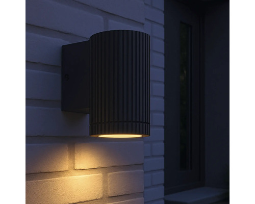 Eine schwarze Aussenwandleuchte ist an einer Backsteinmauer montiert.