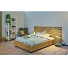 Chambre claire avec lit en bois, lampe de chevet, étagère et fauteuil