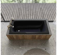 Baignoire noire encastrée dans une étagère avec robinetterie et produit de bain, entourée d''un plancher en bois