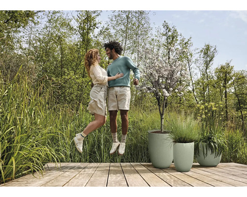 Un couple saute sur une terrasse en bois à côté de trois jardinières.