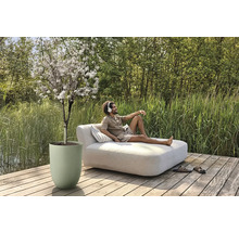 Coin de jardin relaxant avec arbre en fleurs en pot et homme allongé sur un lit de jardin.