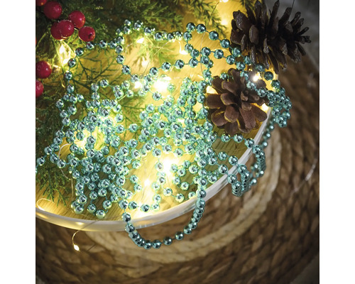 Décoration avec guirlande de boules, branches de sapin, baies rouges, guirlande lumineuse et pommes de pin dans un bol
