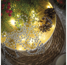 Décoration avec collier de perles argentées, branches de sapin et pommes de pin sur une table ronde.