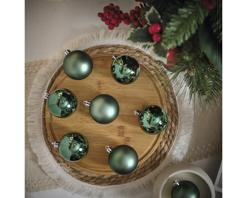 Dekorative grüne Weihnachtskugeln auf einem Holzteller
