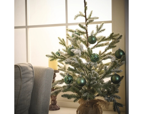 Dekorativer Tannenbaum mit grünen Kugeln und Jutesack auf einem Tisch vor einem Fenster.