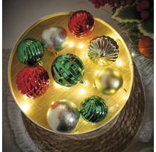 Boules de Noël décoratives en vert, argent et rouge sur une table décorée.