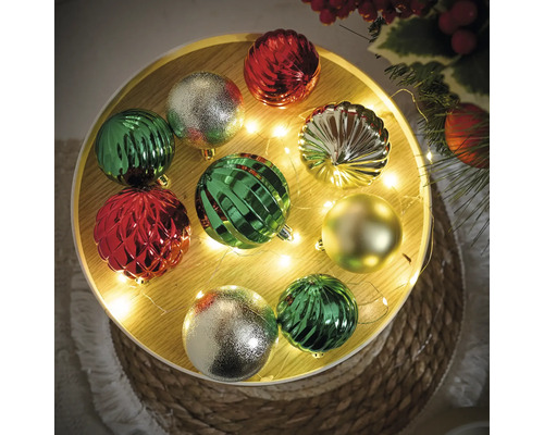 Boules de Noël décoratives en vert, argent et rouge sur une table décorée.