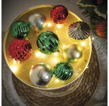 Boules de Noël décoratives en vert, rouge et or sur un plateau rond avec guirlande lumineuse.