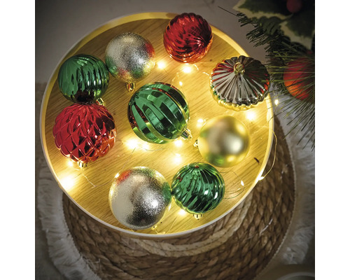 Boules de Noël décoratives en vert, rouge et or sur un plateau rond avec guirlande lumineuse.