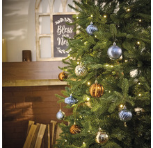 Geschmückter Weihnachtsbaum mit verschiedenen Christbaumkugeln und Lichterkette im Wohnzimmer.