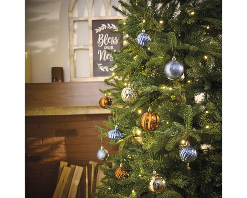 Geschmückter Weihnachtsbaum mit verschiedenen Christbaumkugeln und Lichterkette im Wohnzimmer.