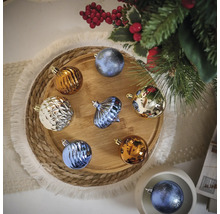 Verschiedenfarbige Weihnachtskugeln auf einem Holztablett neben einem Weihnachtsbaum.