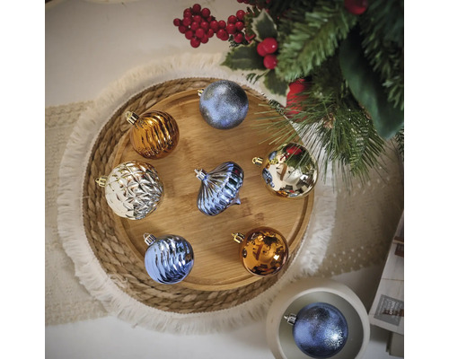 Verschiedenfarbige Weihnachtskugeln auf einem Holztablett neben einem Weihnachtsbaum.