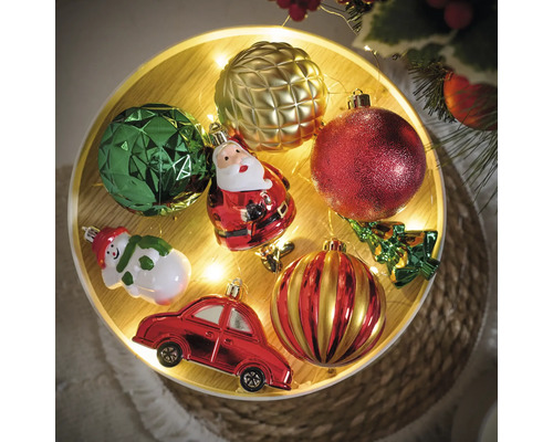 Dekorative Weihnachtskugeln und Figuren auf einem Tablett mit Lichtern.