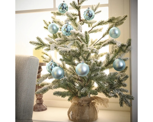 Petit sapin de Noël décoratif avec boules de Noël dans un sac de jute sur un rebord de fenêtre
