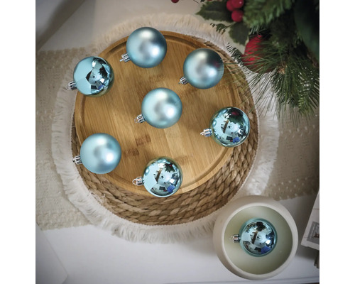 Scène décorative avec des boules de Noël bleues sur une assiette en bois et un dessous de plat tressé