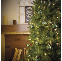 Geschmückter Weihnachtsbaum mit Beleuchtung und Kugeln vor einem Kamin.