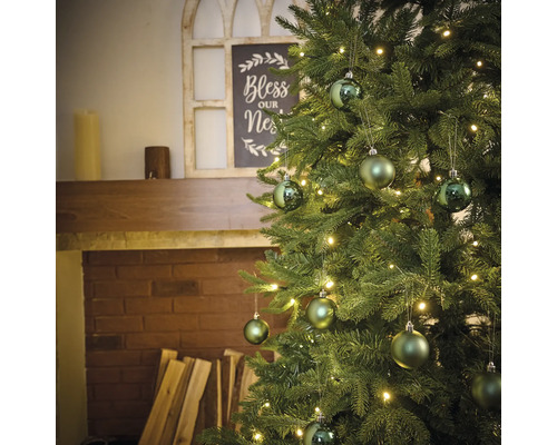 Geschmückter Weihnachtsbaum mit Beleuchtung und Kugeln vor einem Kamin.