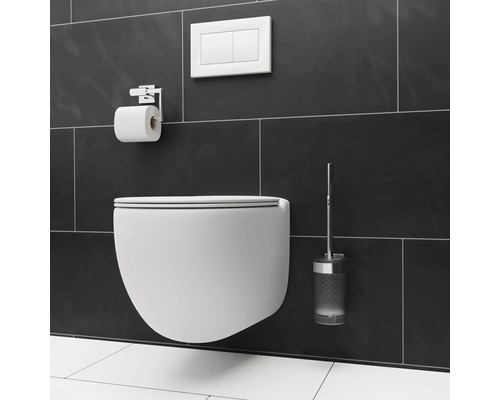 Wandhängendes WC mit Toilettenpapierhalter, Betätigungsplatte und WC-Bürste vor dunklem Fliesenhintergrund.