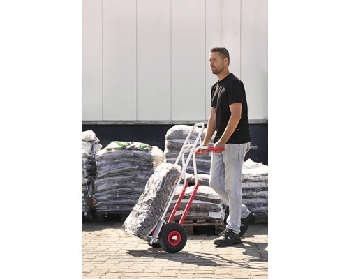 Un homme transporte des marchandises en sac à l''aide d''une diable devant un entrepôt