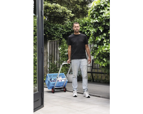 Un homme transporte une caisse à provisions bleue avec un chariot dans le jardin