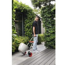 Un homme transporte un pot de fleurs avec un diable dans le jardin.