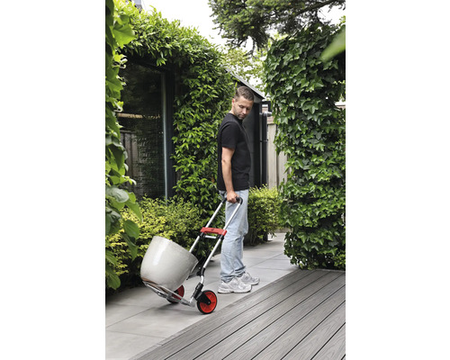 Un homme transporte un pot de fleurs avec un diable dans le jardin.