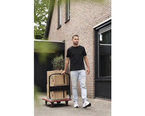 Un homme transporte des cartons de déménagement avec un chariot devant une maison.